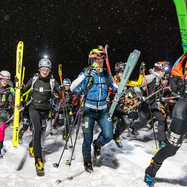 Group of skiers at night in the snow, equipped with skis and ski boots, participating in an event.