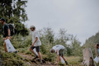 Teilnehmer bei einem Umwelt-Nutzungseinsatz auf einem bewaldeten Hang, tragen Taschen und sind beim Aufräumen oder Sammeln von Abfällen. | © Patron