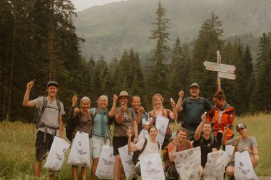 Gruppenfoto während einer Umweltaktion in den Bergen, alle Teilnehmer halten Tüten mit gesammeltem Müll. | © Patron e.V. • Fotograf: Michelle Meitzner